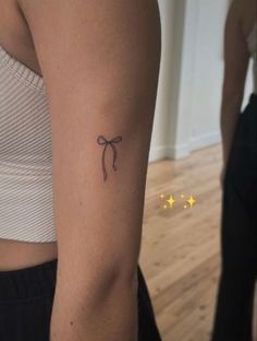 a woman's arm with a small bow tattoo on the left side of her arm