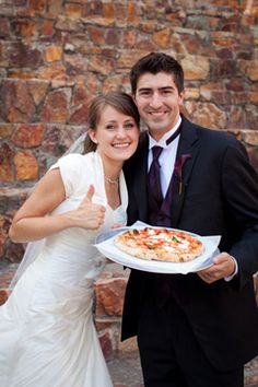 a bride and groom pose with a pizza on their wedding day