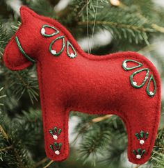 a red felt horse ornament hanging from a christmas tree with green and white ornaments