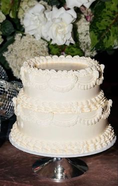 a three tiered white wedding cake sitting on top of a table next to flowers