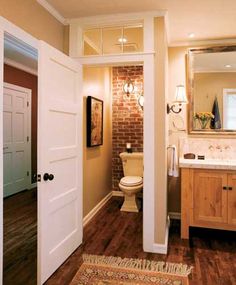 an open door leading to a bathroom with brick wall and wood floors, along with a rug on the floor