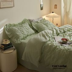 a bed with green sheets and pillows in a bedroom next to a lamp on a table