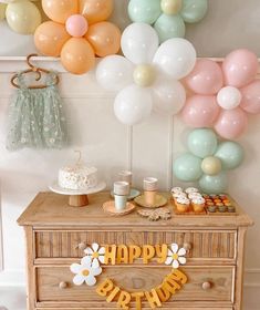 a birthday party with balloons, cake and cupcakes on a dresser in front of the wall