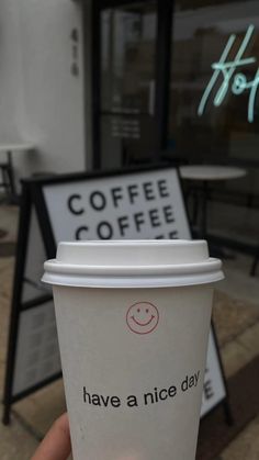 someone holding up a cup of coffee in front of a sign that says have a nice day