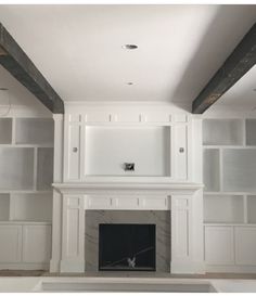 an empty living room with built in bookshelves and white fireplace mantels