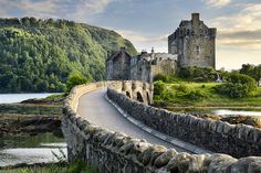 an old castle is on the edge of a body of water near a stone bridge