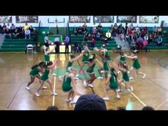 a group of cheerleaders in green outfits dancing on a basketball court while people watch from the sidelines