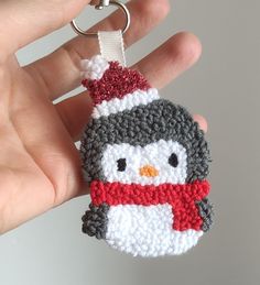 a hand holding a crocheted keychain with a penguin on it