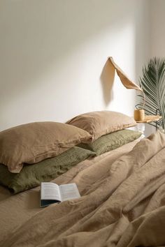 a bed with two pillows and a book on it, next to a palm tree