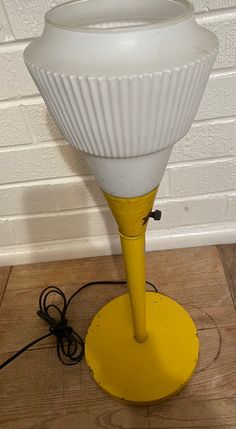 a white lamp sitting on top of a wooden floor next to a wall and power cord