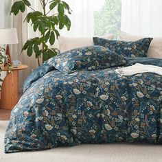 a bed with blue and white comforters in a room next to a plant on the floor