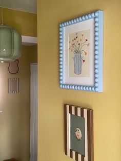 a yellow wall with pictures on it and a blue framed flower vase hanging above the door