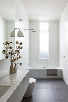 a white bathroom with a tub, toilet and flowers in vases on the counter