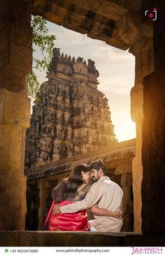 two people are hugging in front of an ancient building with the sun setting behind them