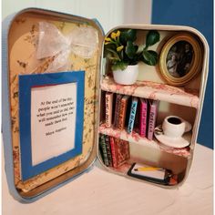 an open tin box with books and other items in it on a table next to a potted plant