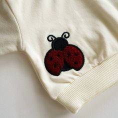 Dress your little Love Bug in our adorable cotton sweater, a perfect blend of charm and comfort. Made from 100% cotton with a lightweight feel, it's ideal for layering or standalone wear. The front boasts a playful 'Love Bug' script, while the back surprises with an embroidered ladybug, adding a pop of whimsy to this sweet piece. Delightfully soft and breathable, the Love Bug Crewneck is a lovable addition to your baby's wardrobe. *please note colors can be different from previous collections du Embroidered Ladybug, Bath Care, Sock Booties, Love Bug, Skirt Jumpsuit, Swim Sets, Love Bugs, Resort Collection, Knit Sweatshirt