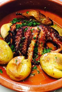 an octopus dish with potatoes and parsley in a clay bowl on a white table