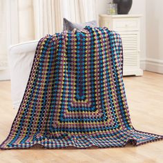 a crocheted blanket sitting on top of a wooden floor next to a white couch