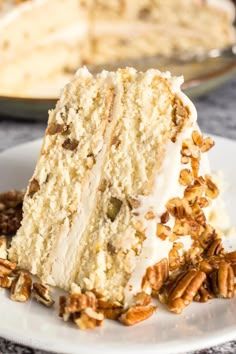 a slice of cake with white frosting and pecans on the side sitting on a plate