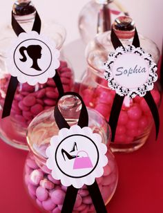 three glass jars filled with candy on top of a pink table cloth covered in candies