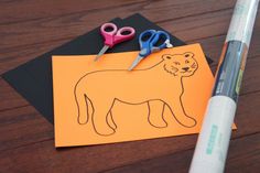 a paper cut out of a lion with scissors next to it on top of a wooden table