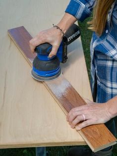 a woman sanding wood with an electric sander on top of the table next to her