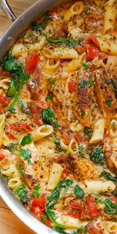 a casserole dish with pasta, spinach and tomatoes in a white sauce