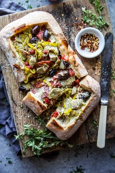 two slices of bread with olives and other toppings on a wooden cutting board