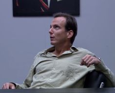 a man sitting at a desk with his arm around the back of his chair and looking off into the distance