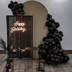 a birthday party with black balloons and a neon sign on the wall behind it that says happy birthday