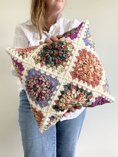 a woman is holding a crocheted pillow in her hands