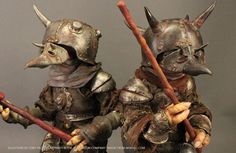 two figurines are dressed in medieval armor and holding spears, both with horns on their heads