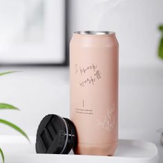 a pink can sitting on top of a white table next to a potted plant