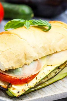 a sandwich with tomatoes, cucumbers and basil on it sitting on a plate