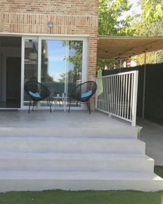 two chairs are sitting on the steps to an outside patio with sliding glass doors and white railings