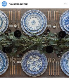 the table is set with blue and white plates, silverware, greenery, and candlesticks