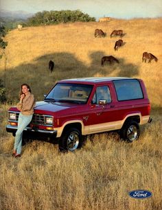 a woman sitting on the hood of a red pick up truck with horses in the background