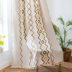 a white and gold blanket sitting on top of a wooden floor next to a potted plant