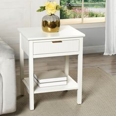 a white end table with a yellow flower on it and a couch in the background