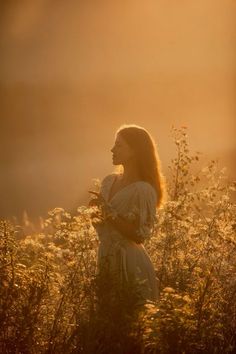 a woman is standing in the middle of a field with tall grass and wildflowers