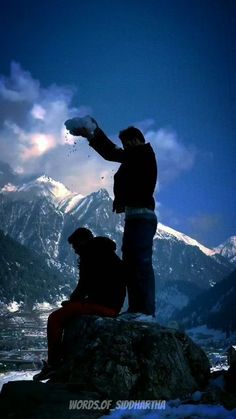 two people standing on top of a mountain with snow covered mountains in the back ground