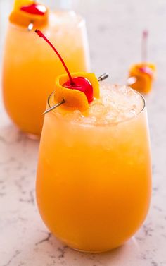 two glasses filled with orange juice and garnished with a cherry on the rim