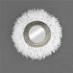 a round mirror with white feathers on the bottom and silver trimmings around it