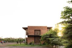 two people walking towards a brick building with trees in the foreground and onlookers