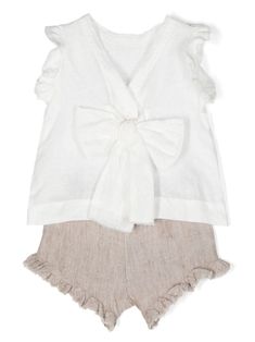 Two-piece set by Il Gufo made of 100% linen consisting of a white flared sleeveless top adorned with ruffles on the armholes. V-neck on the back with button and bow fastening. Matching melange beige linen knickers with elasticated waist and ruching on the leg bottom. The edges of the garment are raw cut and slightly frayed. Ideal garment for elegant occasions or daily looks. Composition: Composition:, 100% Linen. Chic White Linen Sets, White Linen Summer Sets, White Linen Sets For Spring, Linen V-neck Tops With Ruffles, White Sleeveless Ruffled Sets, White Sleeveless Sets With Ruffles, Beach Linen Tops With Ruffles, Beach Tops With Ruffles In Linen, White Linen Beach Sets