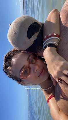 a woman wearing glasses and a hat on top of her head next to the ocean