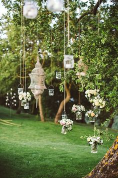 an outdoor wedding with hanging lanterns and flowers on the grass, in front of a tree