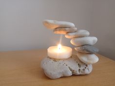 a lit candle sitting on top of a pile of rocks next to a white wall