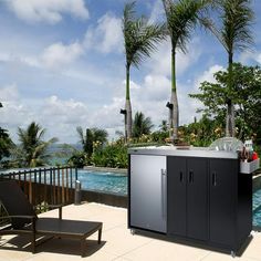 an outdoor bbq next to a swimming pool with lounge chairs and palm trees in the background