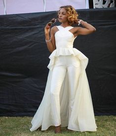 a woman standing in front of a black backdrop with her hands on her hips wearing a white jumpsuit